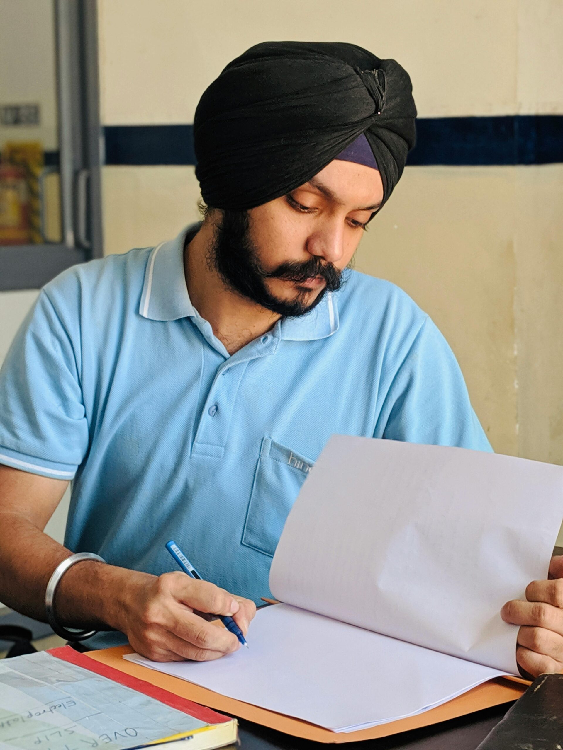 A South Asian man wearing a turban intently studies documents at a desk in India.